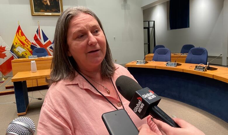 A woman speaks into microphones while standing in Fredericton council chambers.