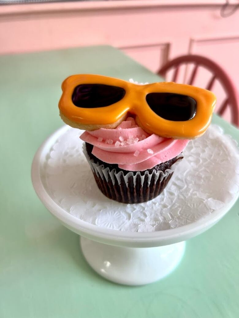 A chocolate cupake with pink frosting and orange sunglasses-shaped cookie on top is pictured sitting on a tray. 