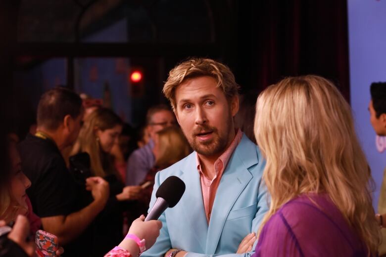 A man wearing a baby blue blazer and pink shirt speaks to reporters at an event.