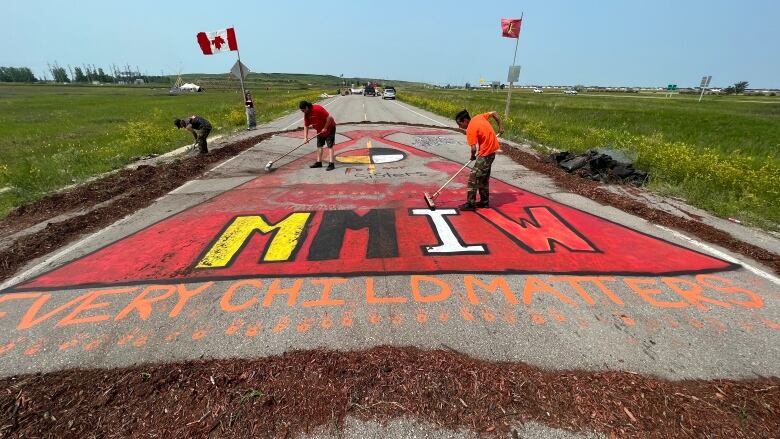 People sweep soil and woodchips off a red dress mural on a road.