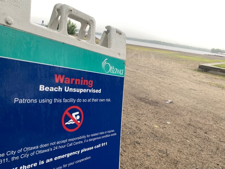 A sign saying a city beach is unsupervised on a cloudy summer morning.