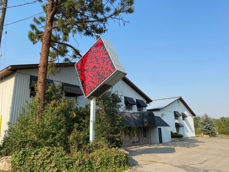 Exterior of a white warehouse with a red QR code sign next to it.