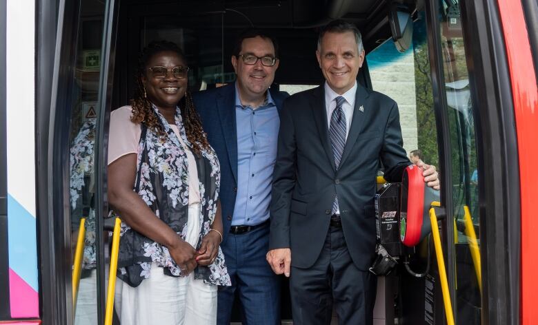 Three smiling people at the front of a bus.