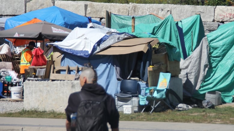 Two people on bicycles are blurry, tents set up on a vacant lot are in focus on the other side of the road from the cyclists