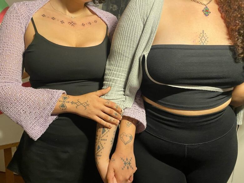 Two women show tattooed arms and chests.