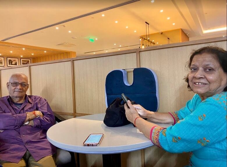 A south Asian man and woman sit smiling on opposites sides of a small round table. 