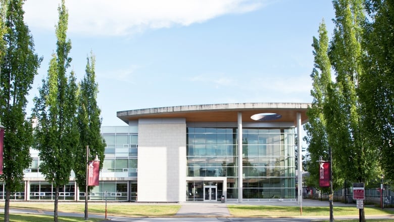 A building with a glass and concrete facade is pictured surrounded by trees. 