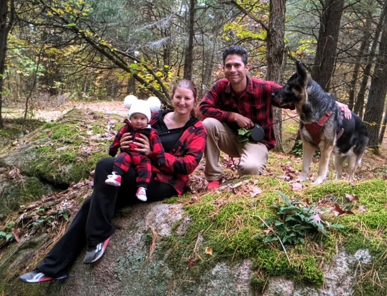 A family of two adults, a small child and a dog pose for a photo outside on a rock.