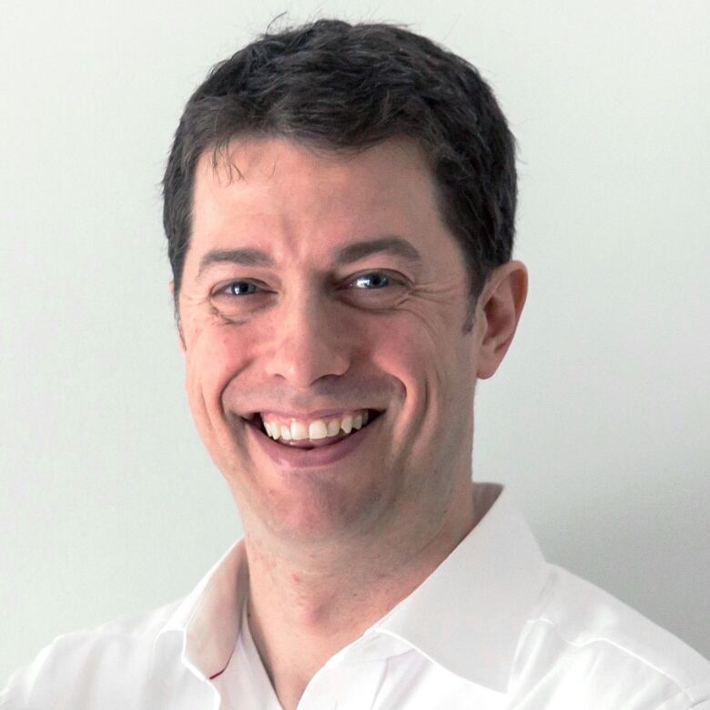 A headshot of a white, middle-aged man with hair smiling. The background is white.