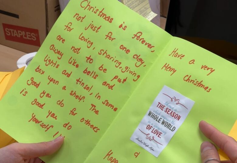 A bright Christmas card with a personal message is held open and read by a volunteer.