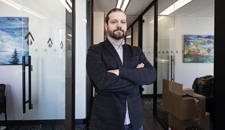 A man wearing a suit jacket in an office, with his arms crossed.