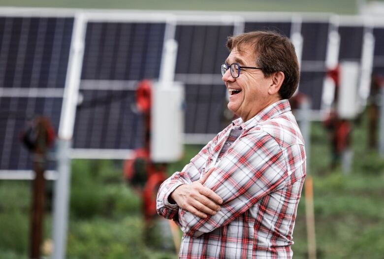 A man in a plaid shirt stands in front of a row of solar panels.