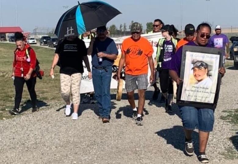 People walk down a gravel road with signs and photos.