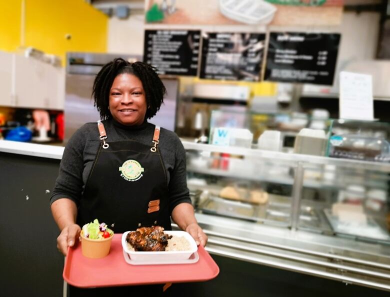 A woman holds a tray of jerk chicken and rice.