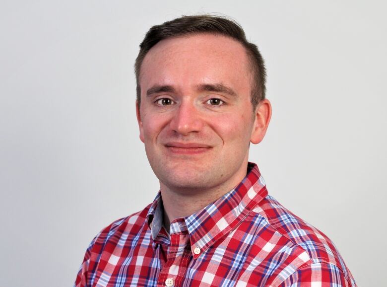 A head shot of a man with brown hair wearing a plaid shirt