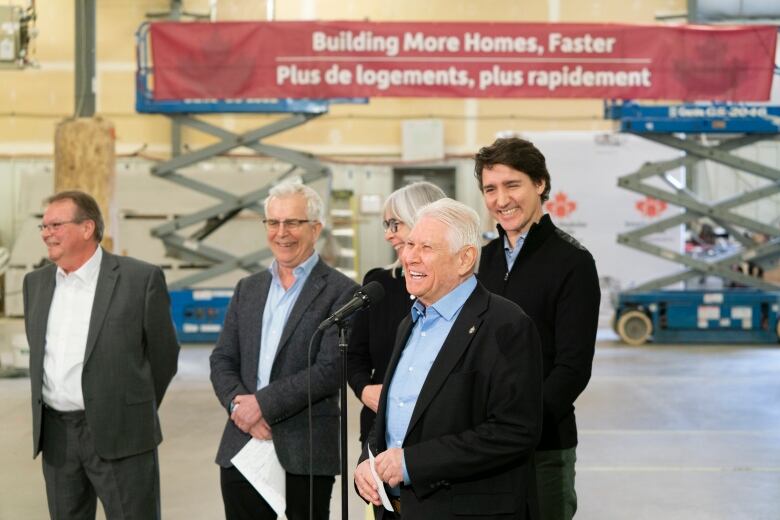 An older man speaks at a microphone. 