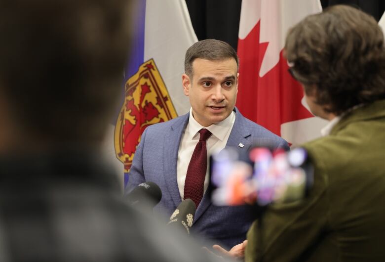 A man in a suit and tie stands in front of flags.