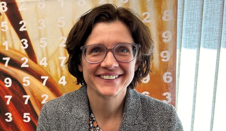 A woman with shoulder-length, brown hair and glasses is pictured smiling.