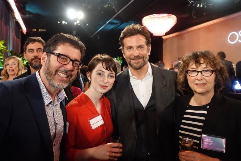 A bearded man wearing glasses, a woman in a red top, a man in a suit and a woman with glasses and curly hair pose for a photo.