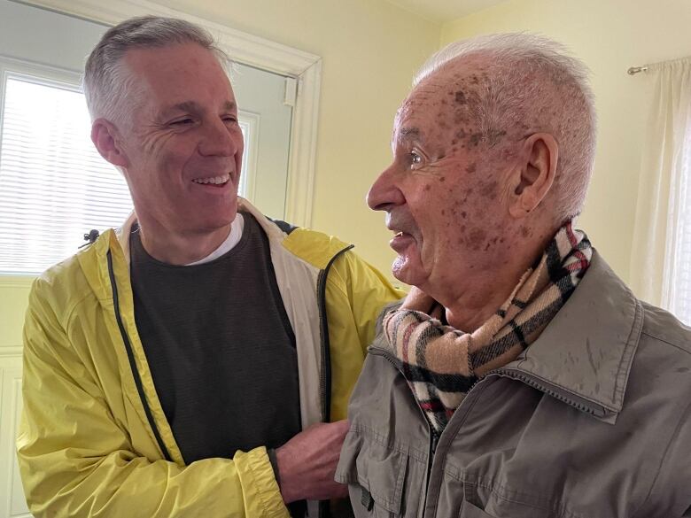 A middle aged man and an elderly man smile at each other.