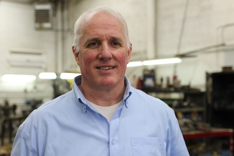 A man in a blue button down and white t-shirt is pictured inside a manufacturing facility.