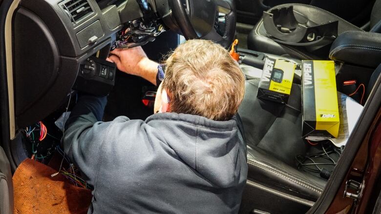 A man installs something under the steering wheel of a car.