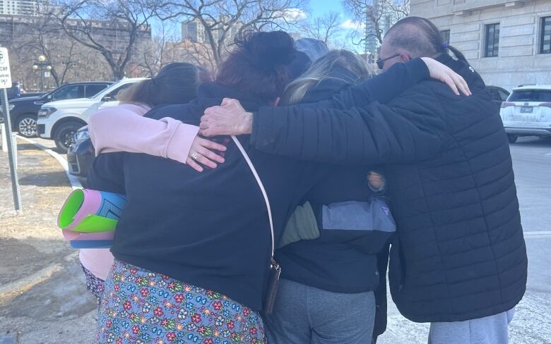 A group of people hugging outside of a building.