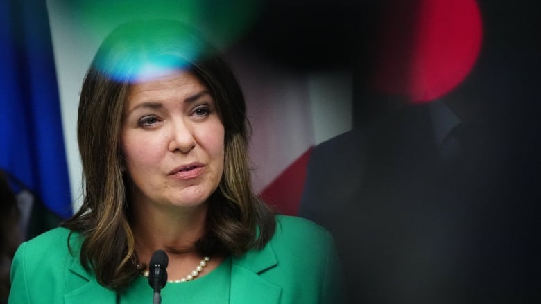 A woman in a green suit wearing a pearl necklace.