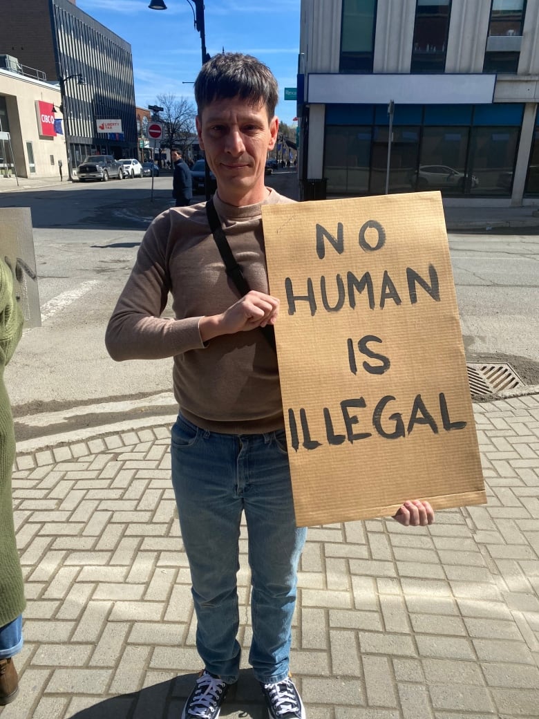 A man stands with a sign reading 'no human is illegal.'