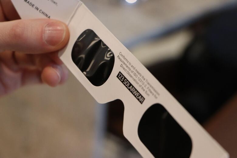 A person holds a pair of eclipse glasses marked with the code 