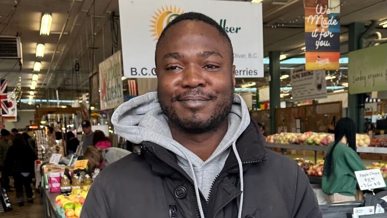 Smiling man stands in front of apple stands at fruit market