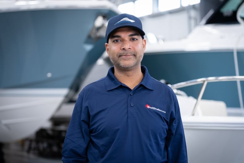 A man in a ball cap and blue, long-sleeved polo poses inside a boat dealership.