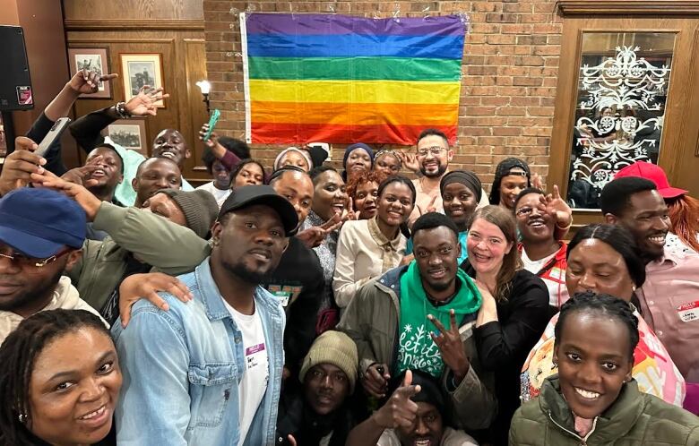 Dozens of smiling people, mostly of African heritage, pose for a group photo in front of a rainbow flag at a bar in Edmonton.