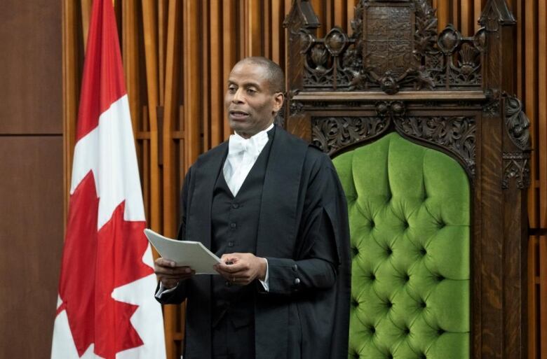 A man in a black rob stands in front of the Speaker's chair in the House of Commons.