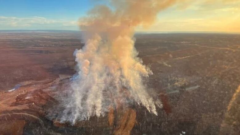 An aerial image of a wildfire shows orange smoke columns billowing into a blue sky.