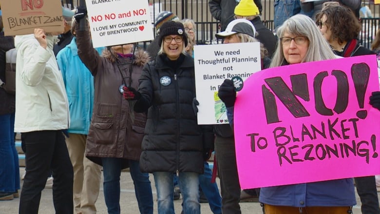 Older people, mostly women, hold signs at a small rally