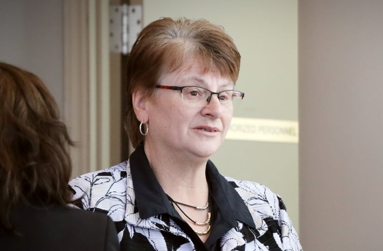 A woman with red hair wearing glasses and a black-and-white print blouse.