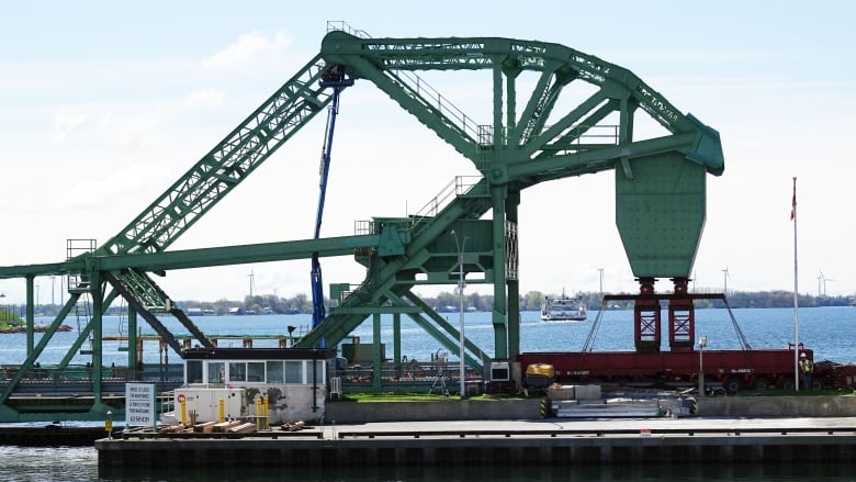 A large green metal bridge with a heavy counterweight being supported by red hydraulic jacks is seen in a photo take from the water.