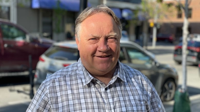 Older man in a plaid shirt stands on a city street.