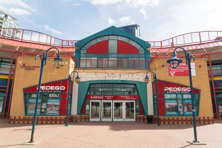 a building is pictured from the outside front entrance. there are light posts in front. it is red and teal coloured metal with orange brick.