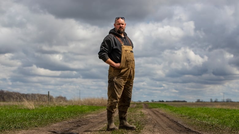 A man stands on a dirt path with fields on either side.