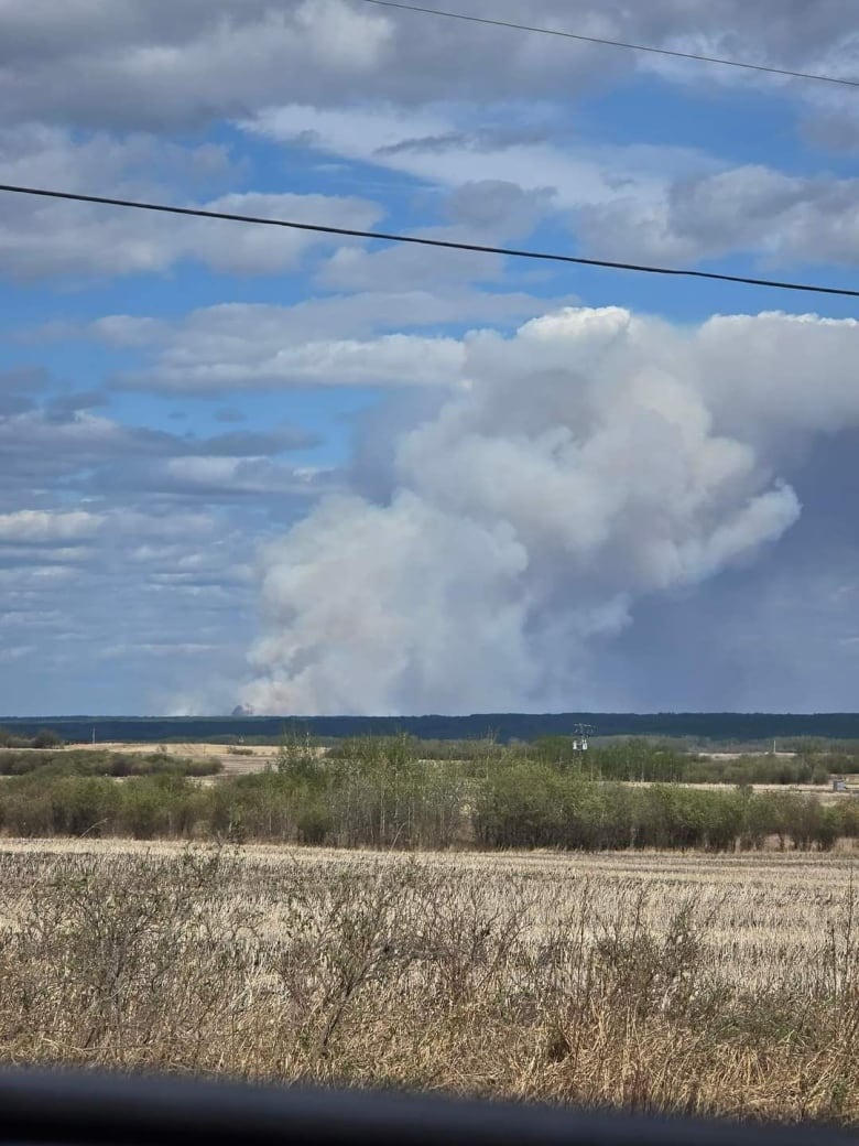 Plumes of smoke rise from a fire on a partly cloudy day.