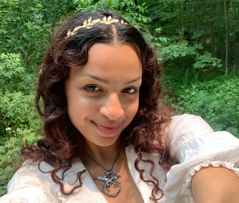 A selfie of a young woman in a white dress in front of some trees.