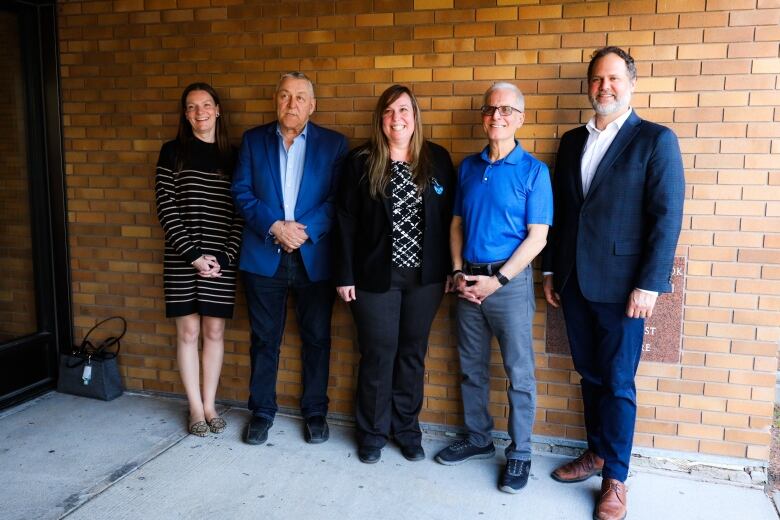 Five people pose for a photo along a brick wall. 