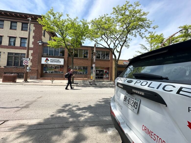 A man walks across the street, as a Windsor Police car sits in the foreground of the image.