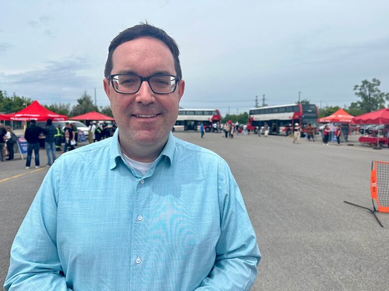 A man stands in a parking lot with public busses behind him. 