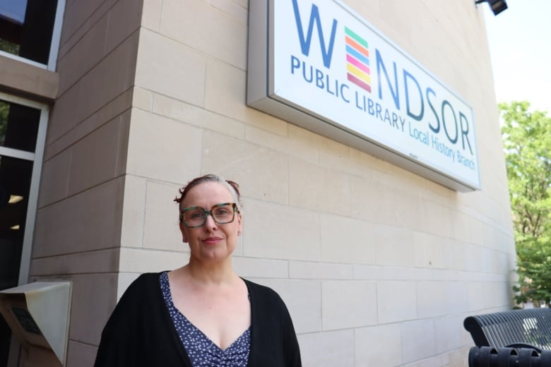 A woman stands outside in front of a big sign that reads, 'Windsor Public Library Local History Branch.'