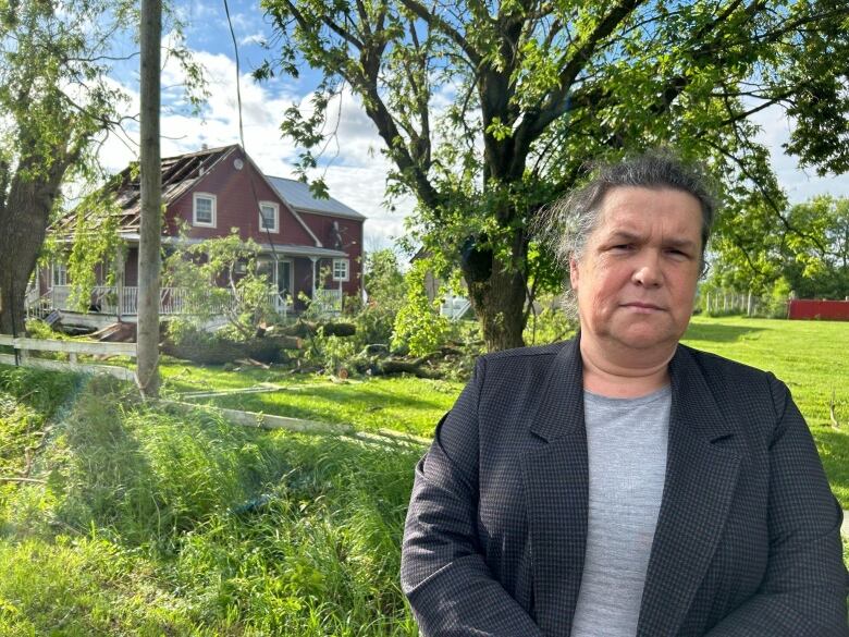 A woman stands in front of a home missing a roof.