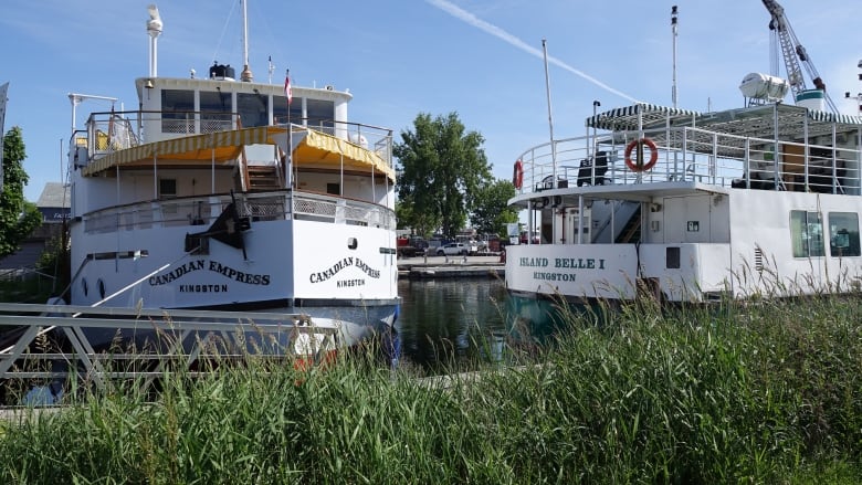 A large red and white passenger boat and a green and white passenger boat are shown next to each other, in the water, on a sunny day.