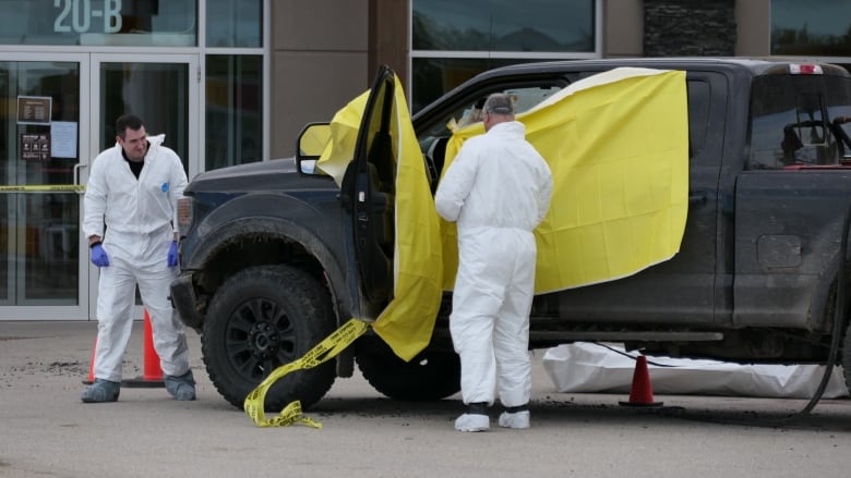 Two men in white garments look through a tarped off truck.